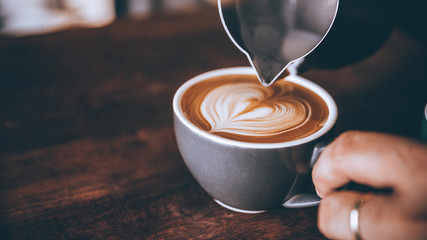 Barista making pouring stream milk with coffee latte art pattern heart shape.