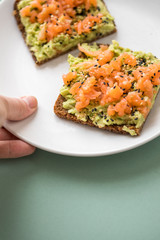 Frau isst Avocado Räucherlachs Vollkorn Sonnenblumenkern Brot und Sesam zum Frühstück auf grünen Hintergrund
