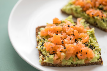 Avocado Räucherlachs Vollkorn Sonnenblumenkern Brot und Sesam zum Frühstück auf grünen Hintergrund