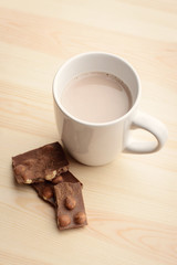 Sweet chocolate drink that is made with cocoa powder stands on wooden table near some pieces of chocolate bar with nuts