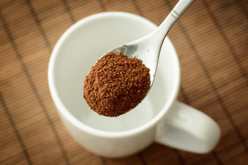 Spoon with ground coffee over the white empty cup against a brown bamboo background. Making coffee