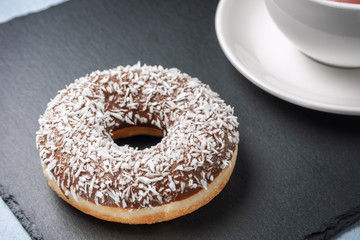 Donat sprinkled with coconut next to a Cup of tea on a slate.