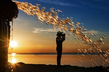 A man photographs the sunset over the water on the background of golden splashes of water