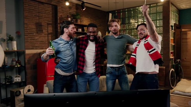 Group of multiracial male friends watching sport game on TV at home and having fun. People watching game at a sports bar cheer for their team. Fans watch a soccer game, and celebrate a successful game