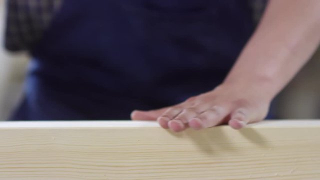 Close up of male hand checking smoothness of wooden plank and then sanding it with orbital sander