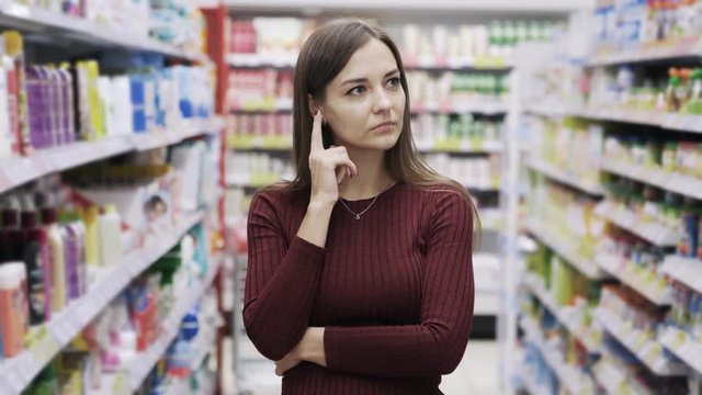 Thoughtful young pretty woman touches her face while she thinks about decision in supermarket