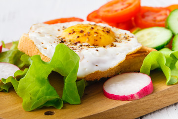 Tasty sandwich toast with avocado, tomato and poached egg on wooden chopping board