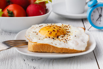 delicious breakfast - hot french toasts, melted emmental cheese and fried sunny side up egg served on a white plate with cup of coffee on a table