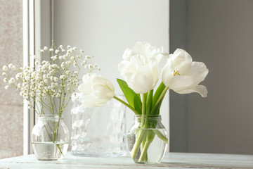 Jars with beautiful flowers on table near window