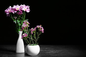 Vases with beautiful flowers on dark background