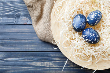 Hand painted dark blue easter eggs in nest and flowers on wooden table