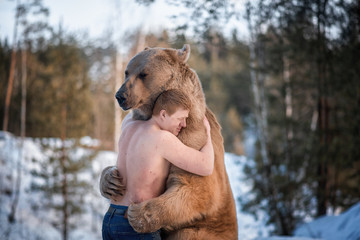 Half-naked man hugs a brown bear in a winter forest. Bear hugs man in response. The theme of the...