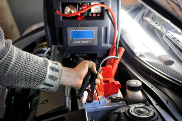 Close up of hand charging car battery with electricity trough jumper cables on the background of the charger
