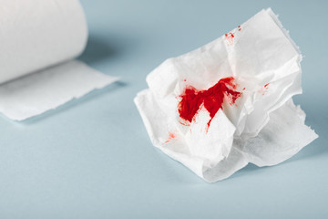 A photo of used bloody toilet paper and a toilet paper roll on the light blue background