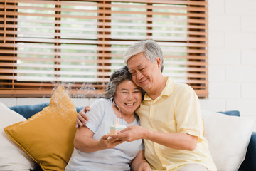 Obraz na płótnie Canvas Asian elderly couple man holding cake celebrating wife's birthday in living room at home. Japanese couple enjoy love moment together at home. Lifestyle senior family at home concept.