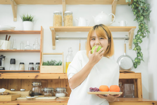 Asian beautiful woman holding fruit and vegetable in the kitchen at her home. Happy pretty asian female eat freshness fruit for healthy body. lifestyle asia woman at home concept.