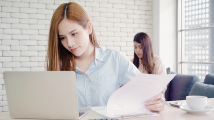 Attractive smart creative Asian business women in smart casual wear working on laptop while sitting on desk on office desk. Lifestyle women work at office concept.
