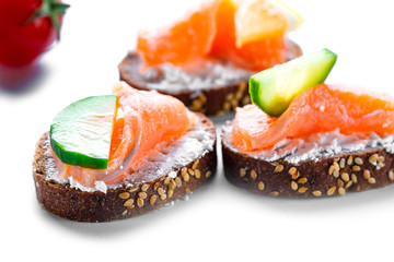 Canape or sandwich with fresh salmon fillet, cucumber and cheese on white background. Finger food snacks for party and banquet