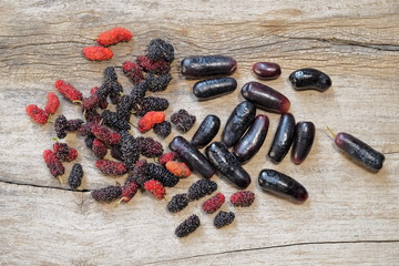 Ripe red and black Mulberry fruit with red wine grapes on wood texture background.