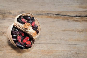 Ripe red Mulberry fruit with red wine grapes mixed in basket on wood texture background.