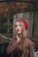 Young beautiful woman in red beret and black dress walks in autumn in the park