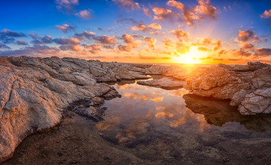 Fototapeta na wymiar Amazing sunset on the white rocks with sun, blue sky, clouds and reflection in the water, Cyprus. Outdoor travel background, panorama