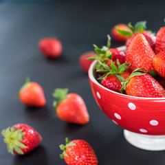 Delicious strawberries in a bowl on black background.
