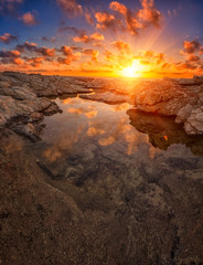 Amazing sunset on the white rocks with sun, blue sky, clouds and reflection in the water, Cyprus. Outdoor travel background, vertical image