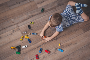 Baby lying on the floor manages multi-colored toy cars