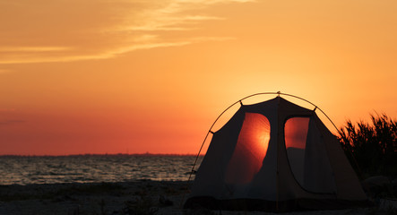 Camping tent on sea beach at sunset in summer