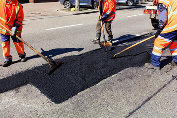 The workers' brigade clears a part of the asphalt with shovels in road construction - obrazy, fototapety, plakaty