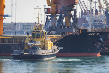 Tugboat at the bow of cargo ship , assisting the vessel to maneuver in Sea Port of Odessa, Ukraine