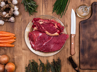 Fresh vegetables on wooden table with two chunks of red meat in centre of the frame