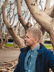 A blond man sitting on a tree with dry twining branches, the roots of which lie on the surface of the Earth