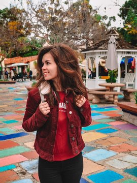 Brunette girl in red jacket and with long hair walks around the Spanish village with bright tiles in the Park in San Diego