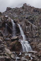Waterfall in a high gorge among the brown rocks and fog of the Altai mountains.