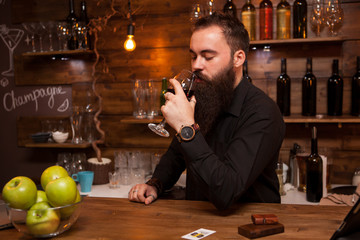 Young tattooed bartender with great beard tasting a glass of wine.