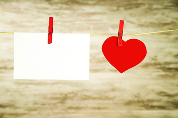 A white card and a red heart hanging on a string, fastened with red buckles