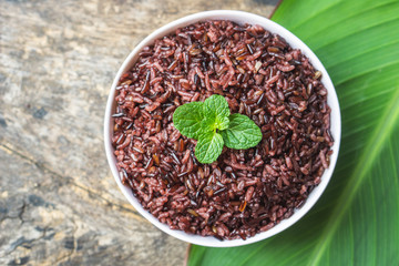 cooked purple rice berry in bowl over green leaf background on wooden table 