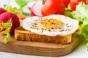 Tasty sandwich toast with avocado, tomato and poached egg on wooden chopping board