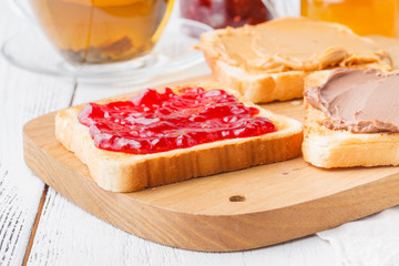 Toast with jam and peanut butter on rustic wooden cutting board - breakfast concept