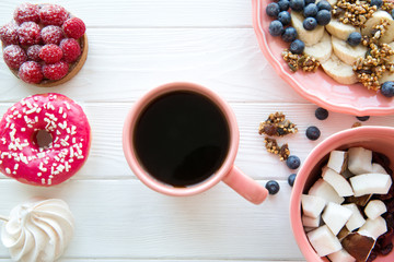 Assortment of delicious desserts, raspberry tart, pink frosted doughnut, pink merengua and banana and coconut pieces in coral color plates on white wooden table. 