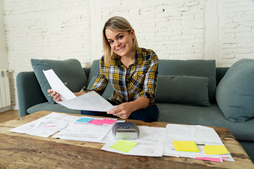 Close up of happy young woman sitting on the sofa surrounded by papers calculating and paying bills