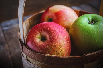 apples with water drops in a basket on wooden background.