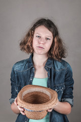 Teens girl with sad face holds an empty straw hat.