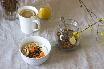 Breakfast of granola with yogurt and tea and forsythia flowers on a linen tablecloth. Rustic style.