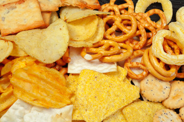 Mix of snacks : pretzels , crackers , chips  and nachos on the table