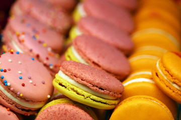 Macaroons in a row, colorful sweet background. Pink, yellow and orange almond cookies with filling, bright colours