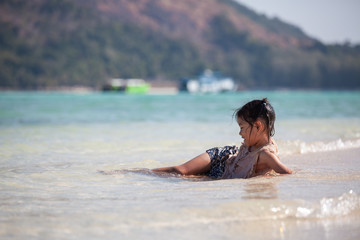 Fototapeta na wymiar Happy asian child girl having fun to play water in the beautiful sea in summer vacation