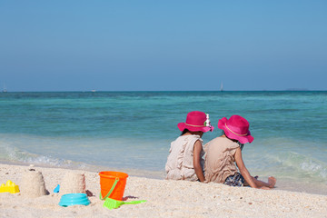 Fototapeta na wymiar Two cute asian little child girls sitting and playing with sand together on the beach near the beautiful sea in summer vacation